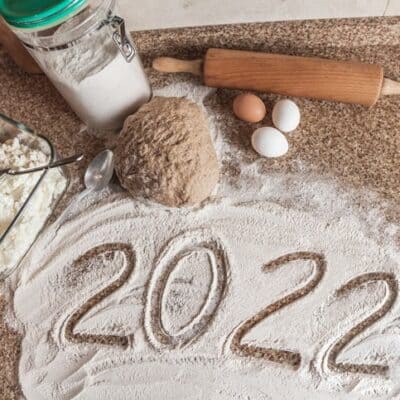 2022 is written in flour. A piece of dough, eggs and a wooden rolling pin lies on a granite countertop JM Kitchen & Bath Design