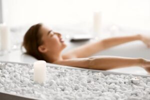 Woman relaxes in a tub with white stones around it--it's her dream bathroom JM Kitchen & Bath Design