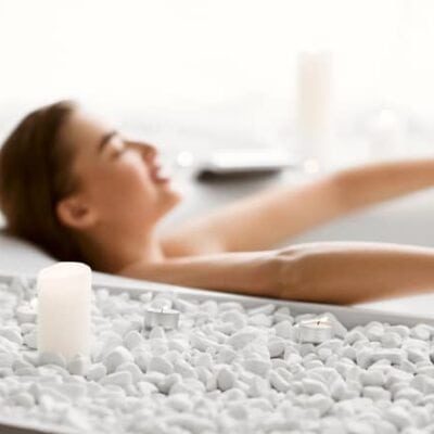 Woman relaxes in a tub with white stones around it--it's her dream bathroom JM Kitchen & Bath Design