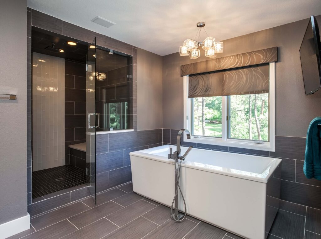 modern bathroom remodel from JM Kitchen & Bath Design features rectangle free standing tub, dark tile and walk-in shower