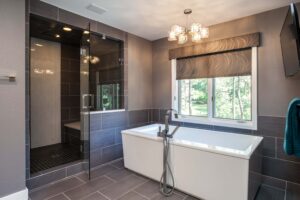 modern bathroom remodel from JM Kitchen & Bath Design features rectangle free standing tub, dark tile and walk-in shower