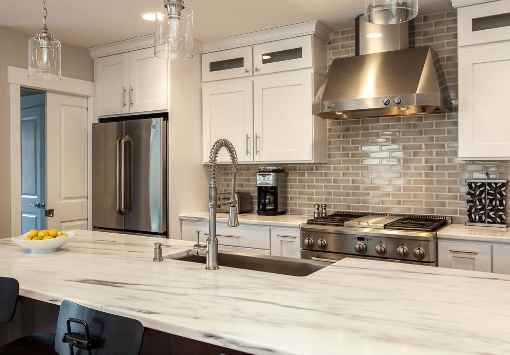 remodeled kitchen features white cabinets, smoky backsplash tile, and off white countertops JM Kitchen & Bath Design