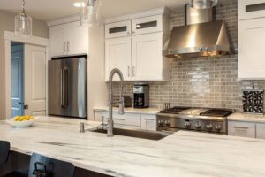 remodeled kitchen features white cabinets, smoky backsplash tile, and off white countertops JM Kitchen & Bath Design