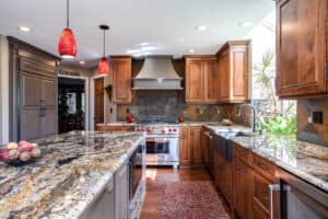 custom granite counter tops with copper, gray, and black accent, oven with red buttons, red scone lighting above island and apron sink are features in kitchen remodel JM Kitchen & Bath Design