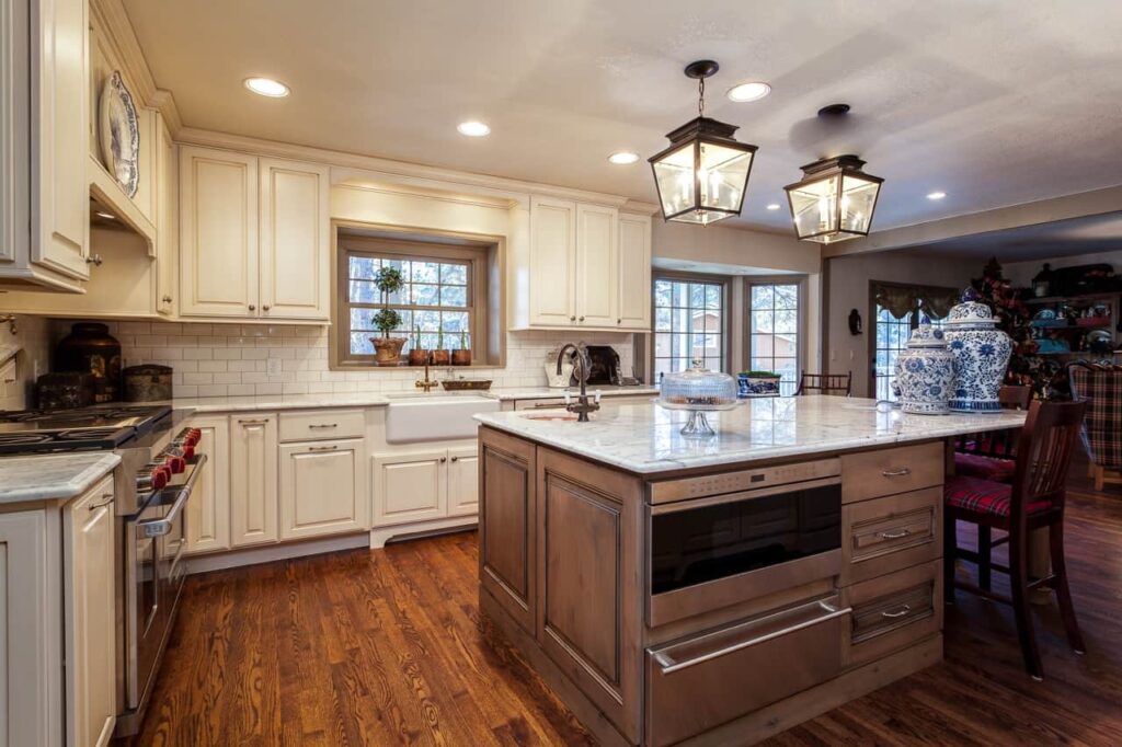 kitchen remodel from JM Kitchen & Bath Design features appliances under island, apron sink, and lantern lighting