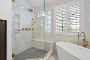 bathroom remodel includes shower with glass door, light gray tile, and matte brass hardware JM Kitchen & Bath Design