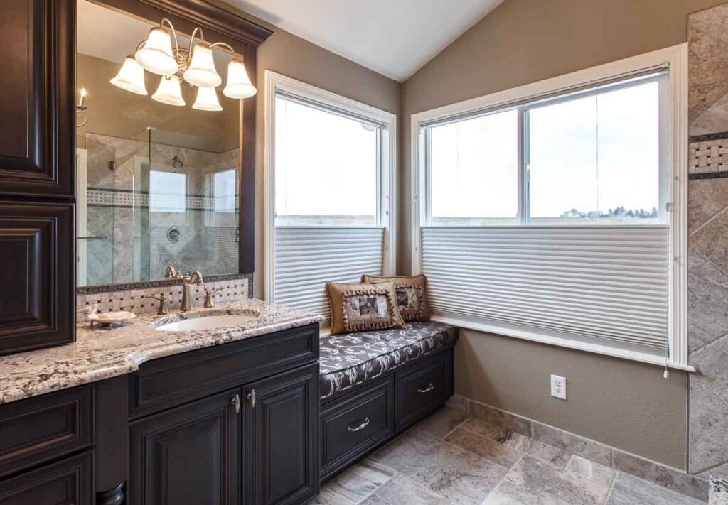 remodeled bathroom from JM Kitchen & Bath Design features privacy blinds, bench, and dark wood cabinet finishes