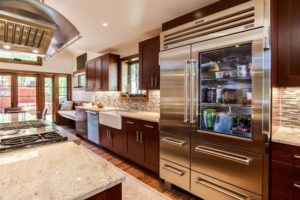 remodeled kitchen features large refrigerator, gas stovetop with large hood and dark wood cabinets JM Kitchen & Bath Design