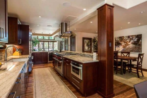 JM Kitchen & Bath Design remodeled kitchen featuring large hood over modern gas stove, apron sink, and dark cabinet finishes