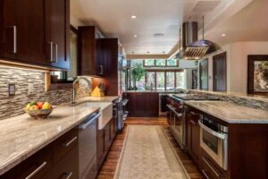 galley view of new kitchen remodel featuring new appliances, dark cabinets, large hood and apron sink JM Kitchen & Bath Design