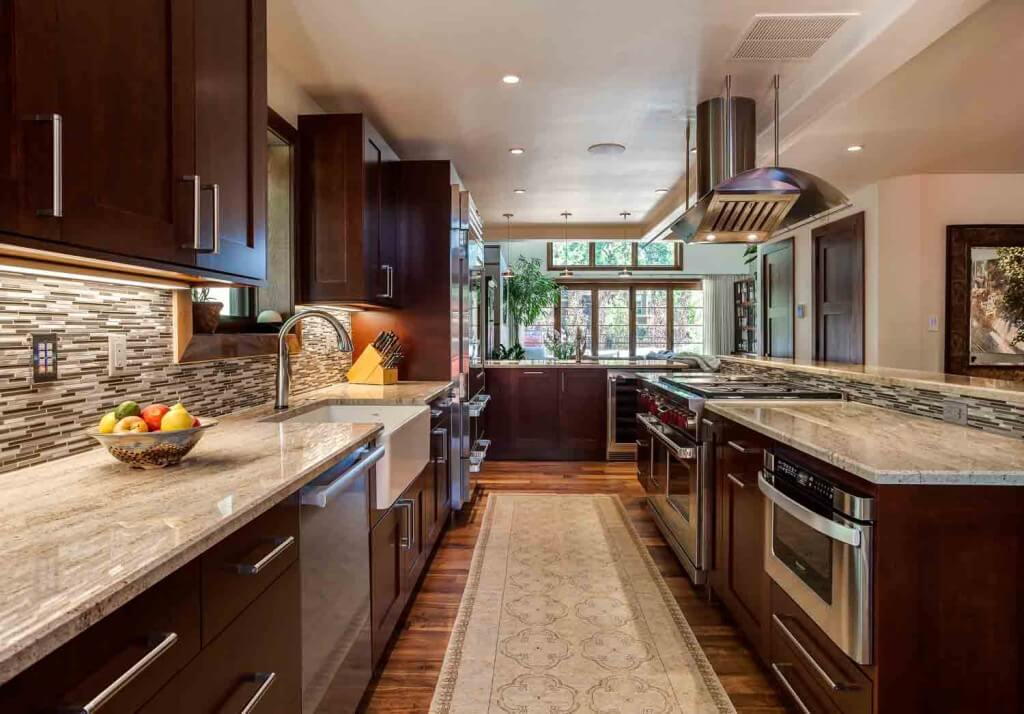 galley view of new kitchen remodel featuring new appliances, dark cabinets, large hood and apron sink JM Kitchen & Bath Design