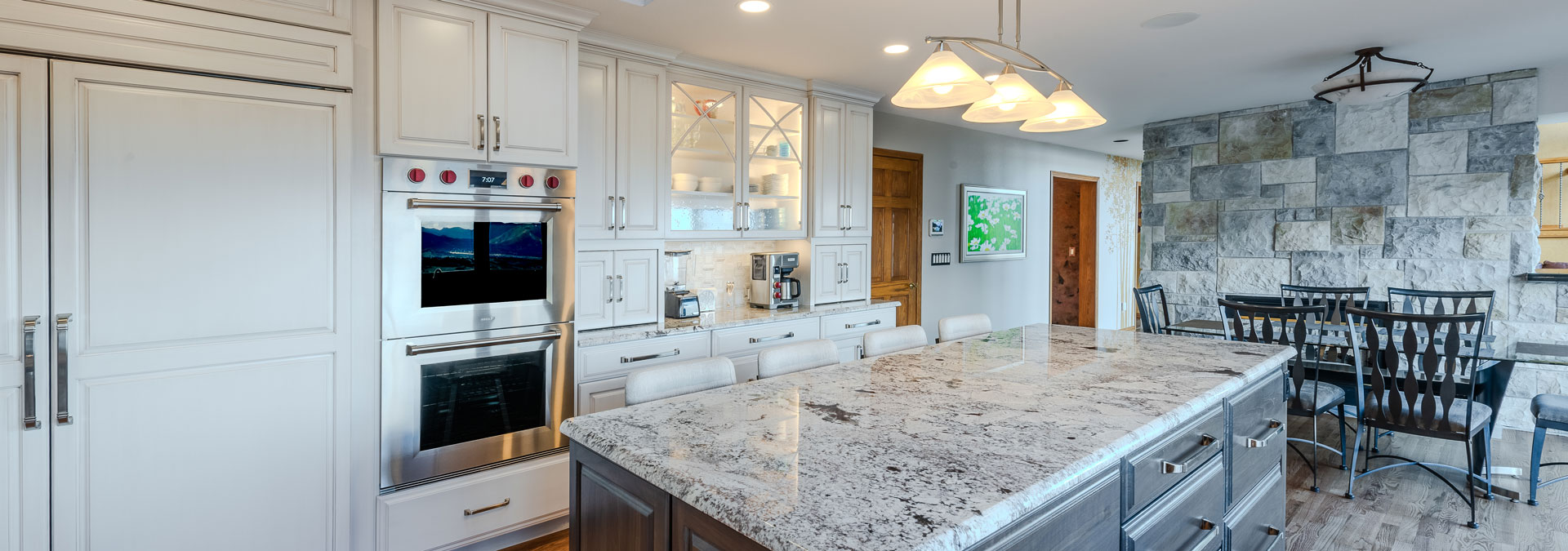 modern remodeled kitchen from JM Kitchen & Bath Design featuring a stone wall, updated countertops, island, and modern lighting