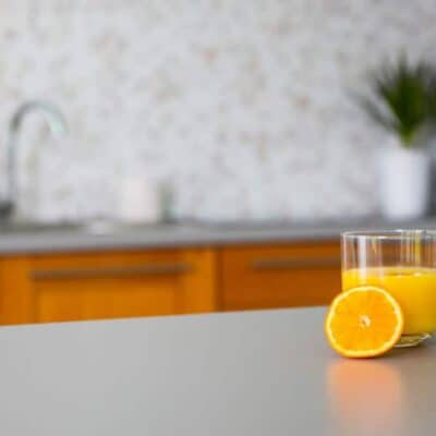 close up of orange juice in glass with slice of orange next to it on kitchen countertop JM Kitchen & Bath Design